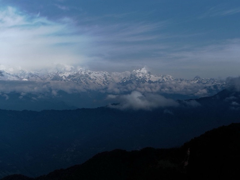 Snow-capped Kanchenjunga range rising above clouds and blue ridges