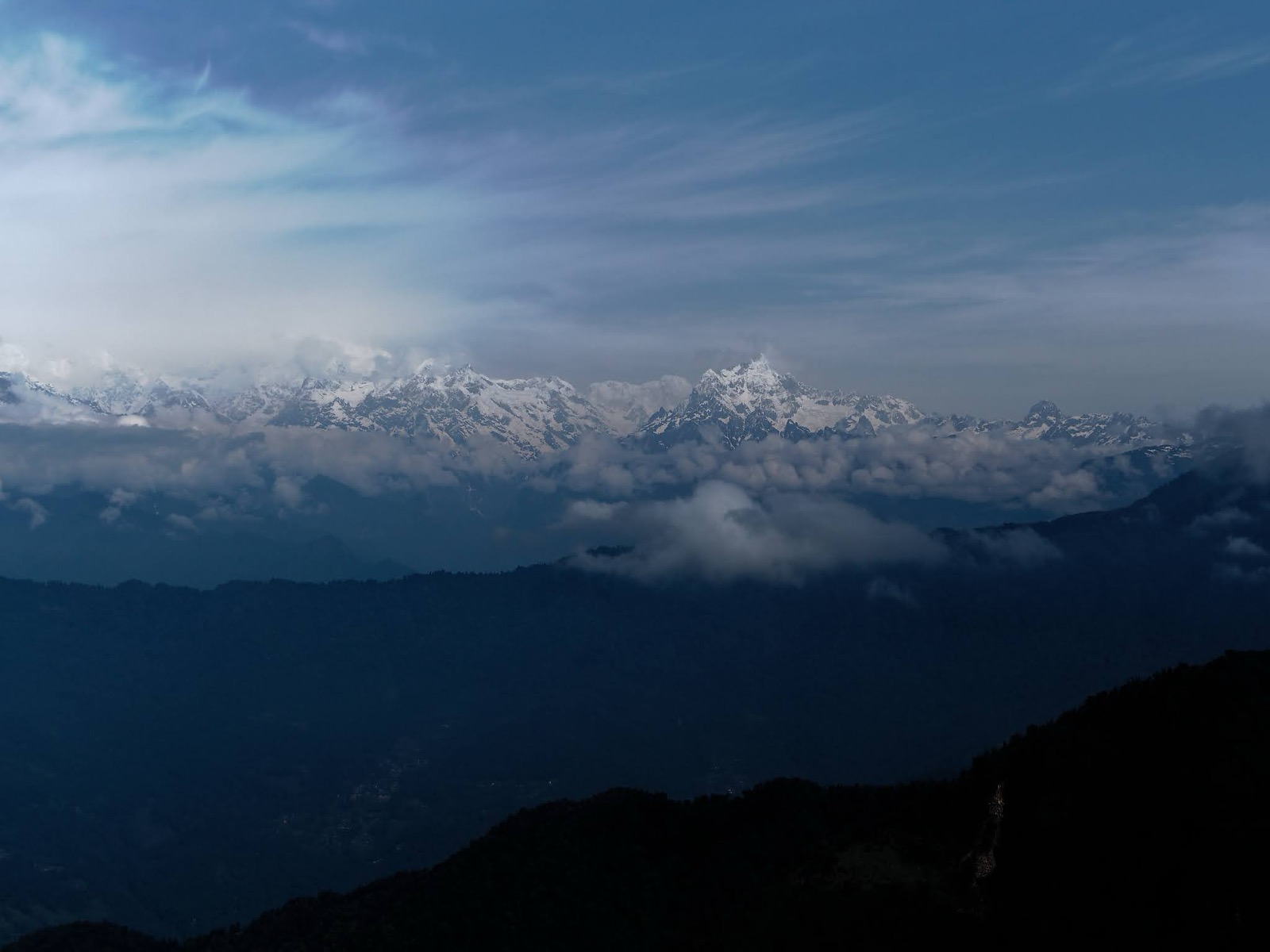 Snow-capped Kanchenjunga range rising above clouds and blue ridges