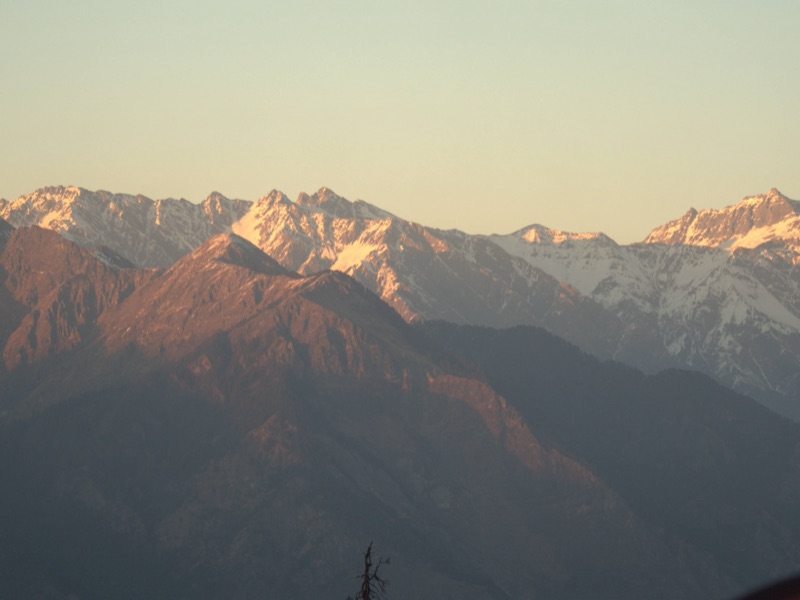 Mountain ridges glowing warm orange at sunset from Kedarkantha base camp