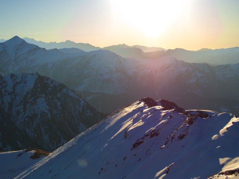 Sunrise over snow-covered summit with mountains stretching to the horizon