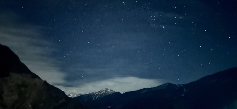 Starry night sky over snow-capped mountain silhouettes from Sankri village
