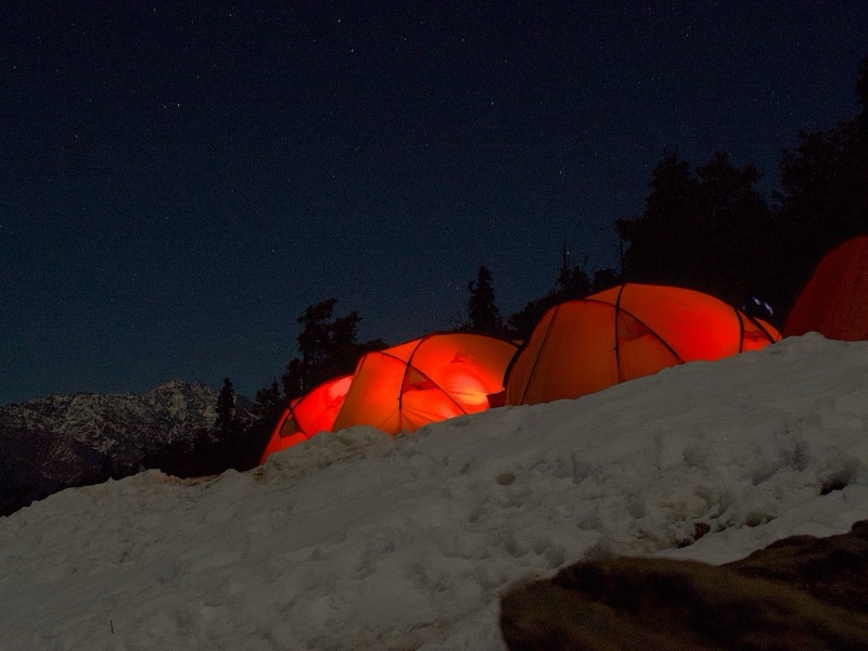 Orange camping tents glowing in snow under a starry night sky